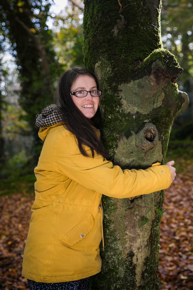 Katie McGreal | Founder Solas Relaxation hugging a tree in the woods.